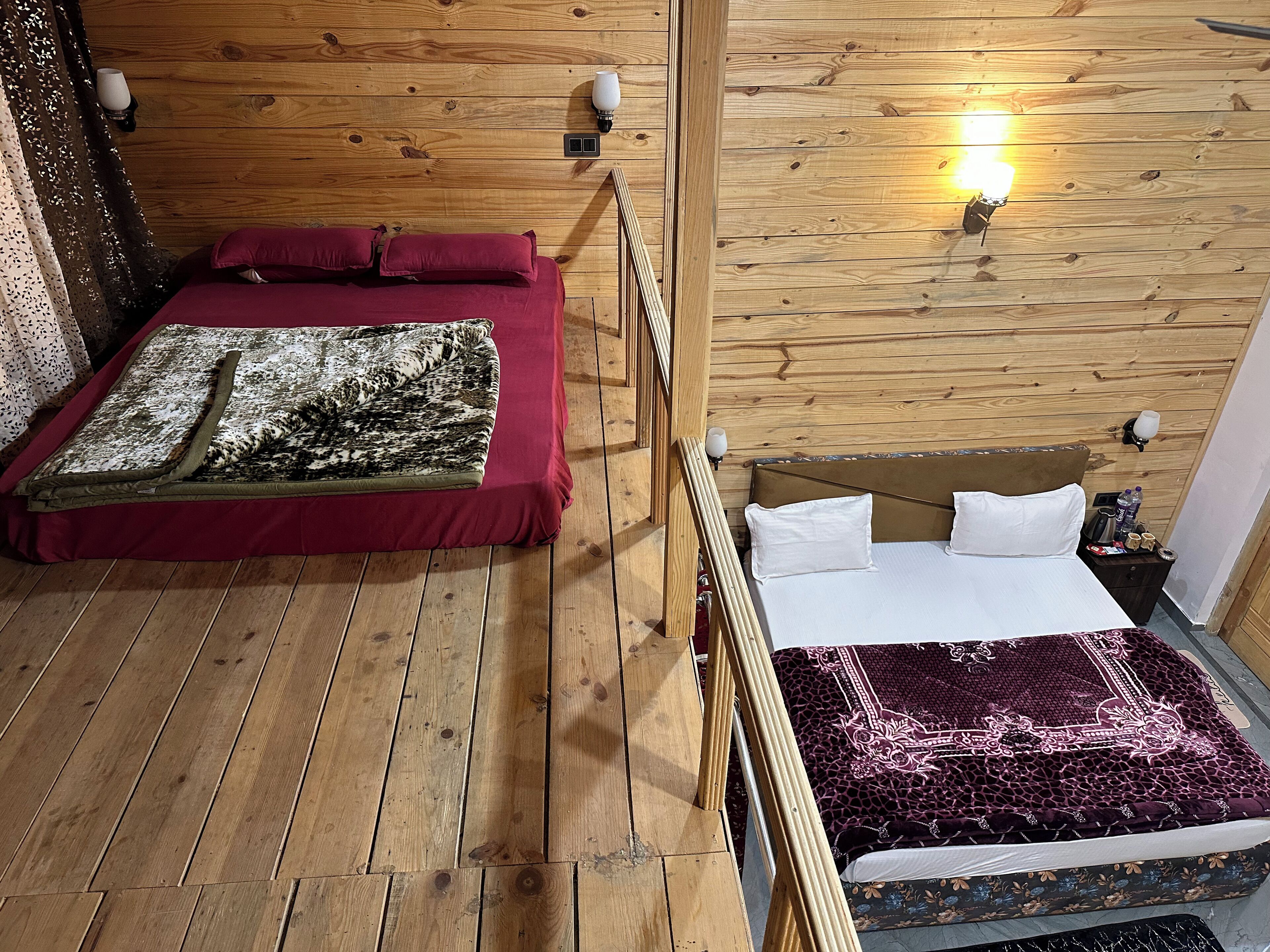 Habitación con paneles de madera y dos camas, una con colcha roja y la otra con colcha blanca.