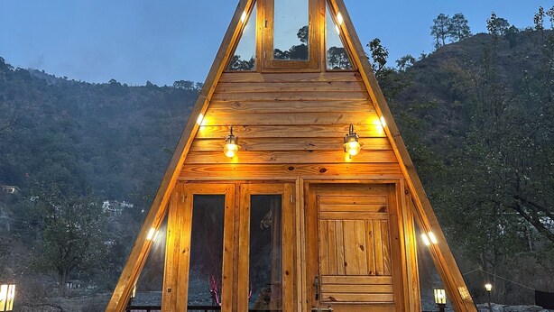 Eine hölzerne, dreieckige Holzhütte mit einem zentralen Fenster und zwei Seitenfenstern, umgeben von einem Metallgeländer.
