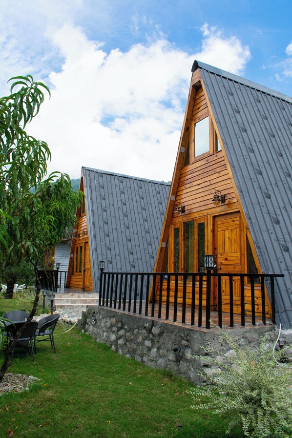 A row of wooden cabins with sloped roofs and a stone pathway leading to the entrance. - Cabana Riverside Resort - Kainchi Dham (Kosiyakutoli)