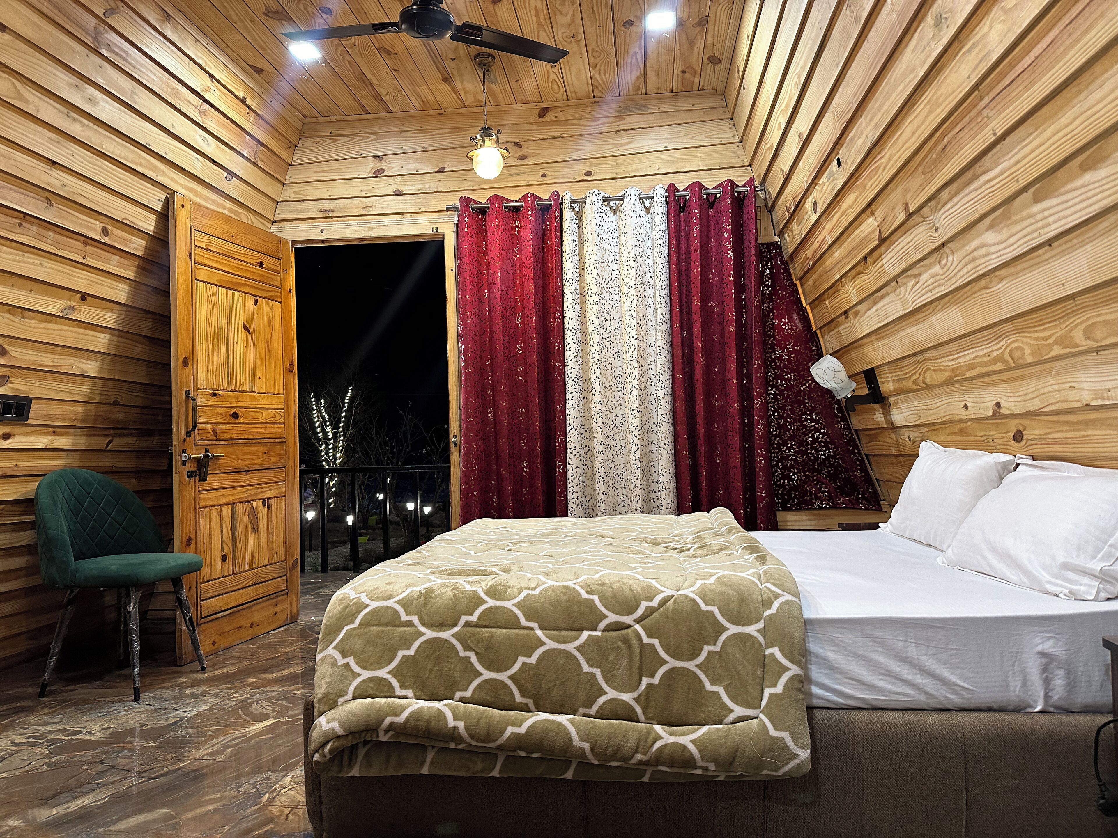 Un dormitorio de cabaña de madera con una cama, una silla y una ventana con cortinas.
