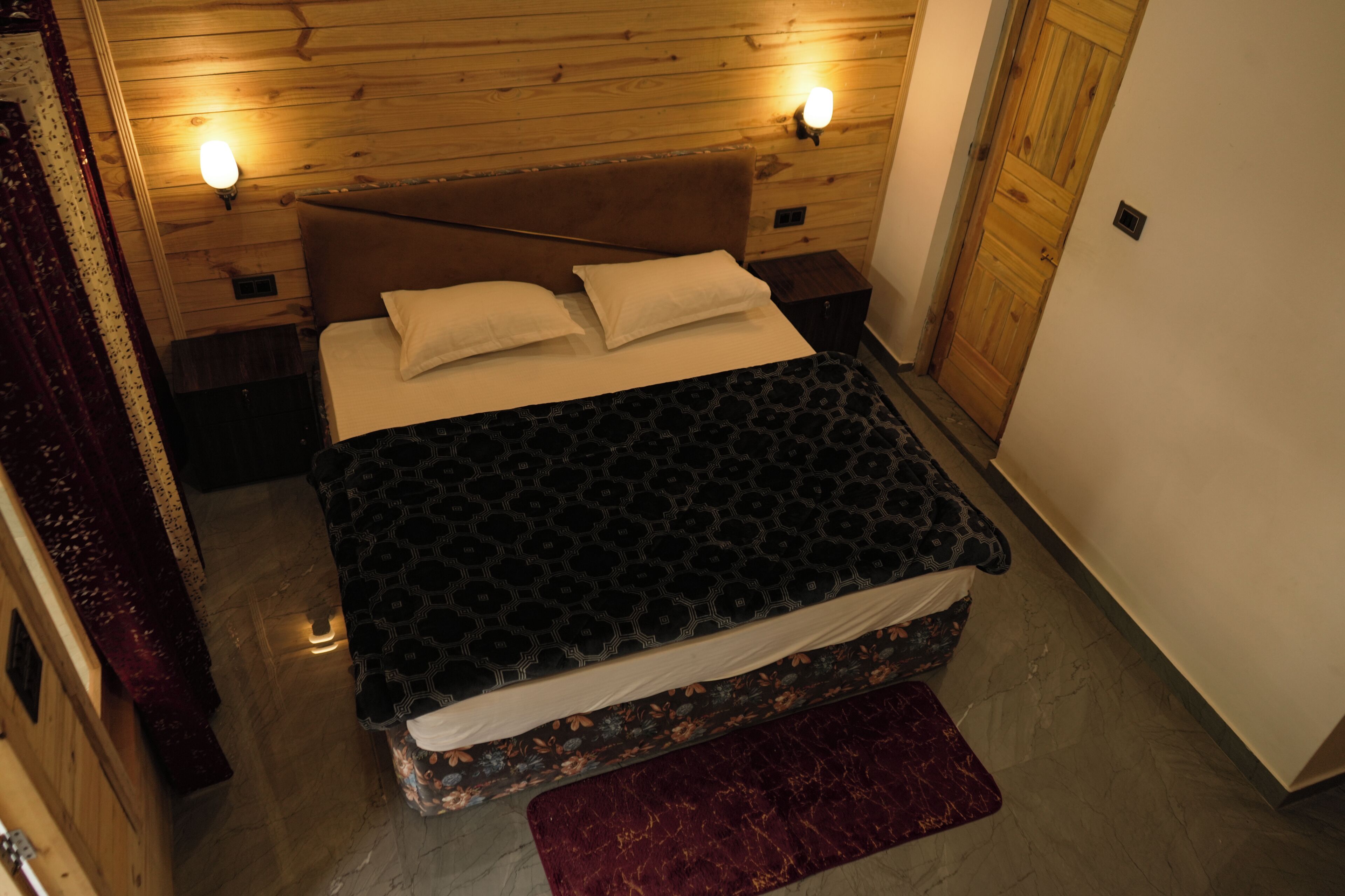 Ein Schlafzimmer mit einem Holzkopfteil, zwei Nachttischlampen, einer gemusterten Bettdecke und einem roten Teppich.