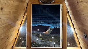 Eine Holzhütte mit geneigtem Dach, Deckenventilator und Fenster mit Blick auf eine verschneite Landschaft.