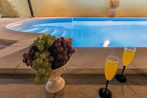 A poolside setting with a decorative bowl of mixed grapes and two glasses of orange juice. - Villa Monique in Vodnjan (Vodnjan)
