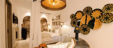 A modern hotel room with a curved sofa, a small wooden table, a round coffee table, and a wall decorated with woven art pieces.
