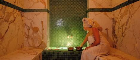 Un baño de mármol con bañera, una pared de mosaico verde y una toalla en el borde.