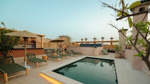 Un espace piscine agrémenté de chaises longues et de parasols, entouré d’une terrasse carrelée et d’un mur en pierre.