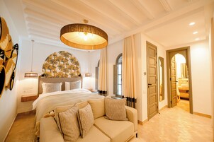 A hotel room with a large bed, a sofa, a chandelier, and a mirror.