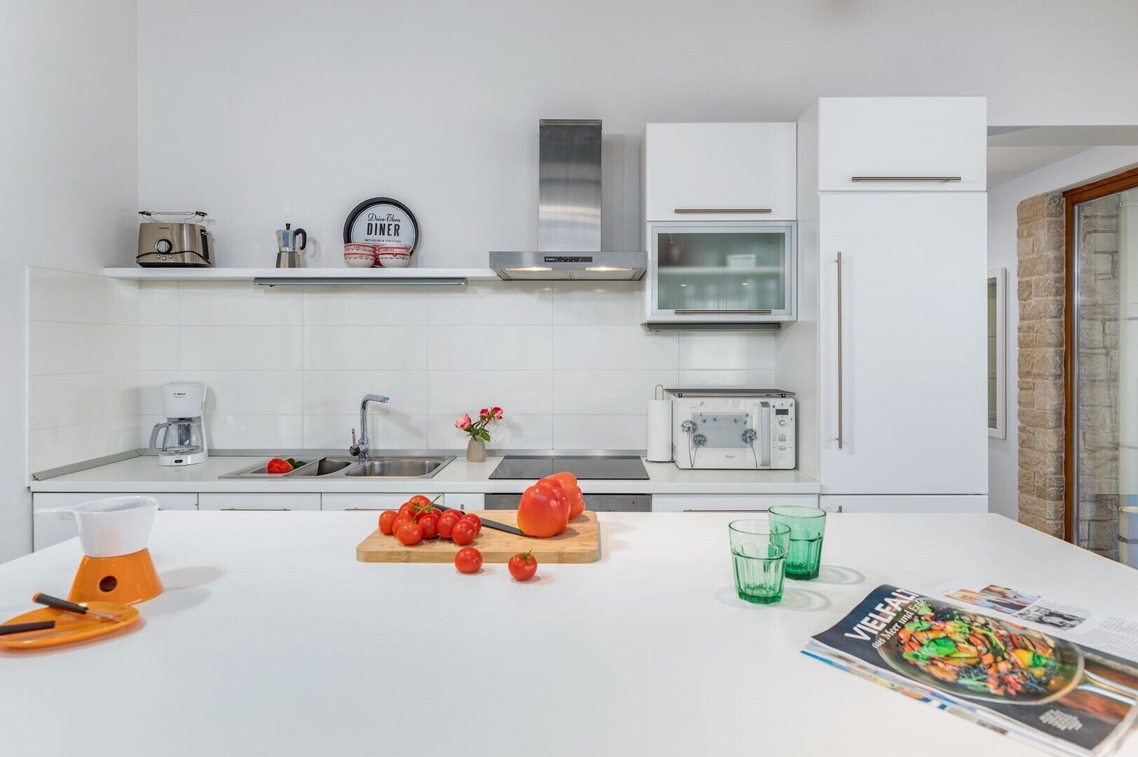 Une cuisine moderne avec des meubles blancs, une hotte en acier inoxydable, un four à micro-ondes encastré et une machine à café.