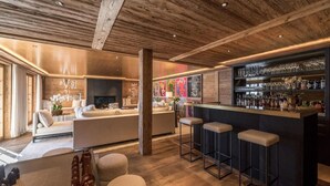 A modern bar area with a wooden ceiling, a bar counter with stools, and a seating area with sofas and a fireplace. - Spacious Chalet With Private Pool (Saanen)