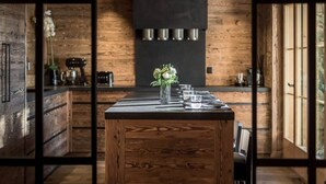 A modern kitchen with wooden walls, a central island with a vase of flowers, and a black backsplash. - Spacious Chalet With Private Pool (Saanen)