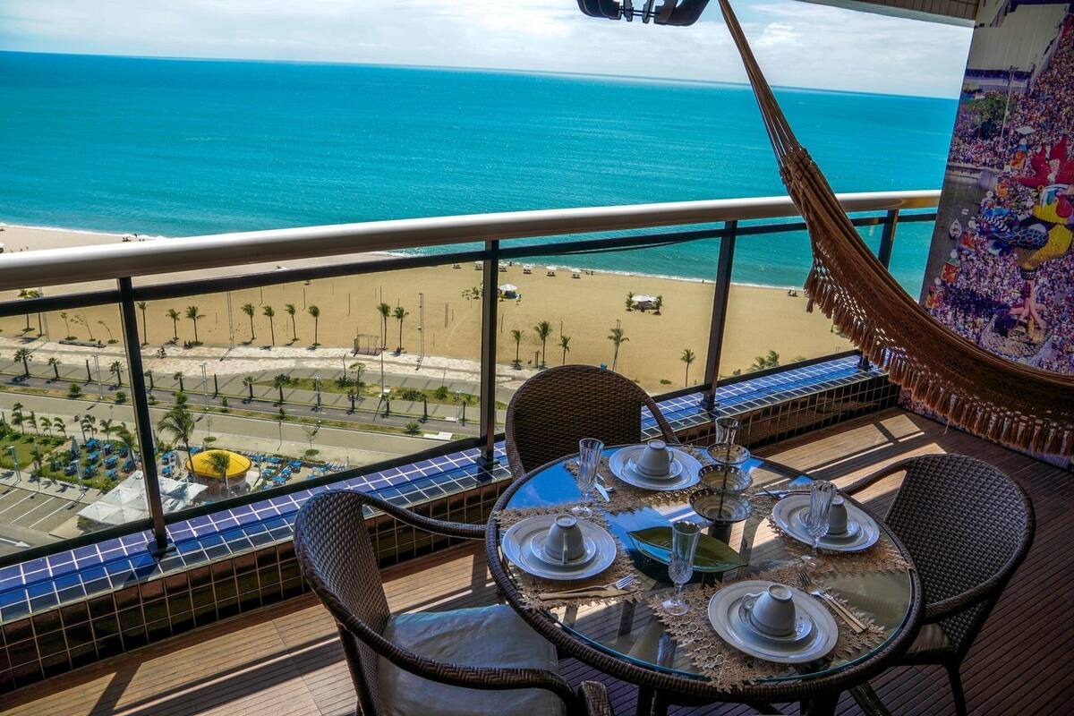 Ein Balkon mit Esstisch, der Blick auf einen Strand und den Ozean bietet.