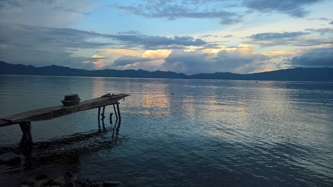 Une jetée en bois s’étendant sur un lac paisible, avec des montagnes en arrière-plan.