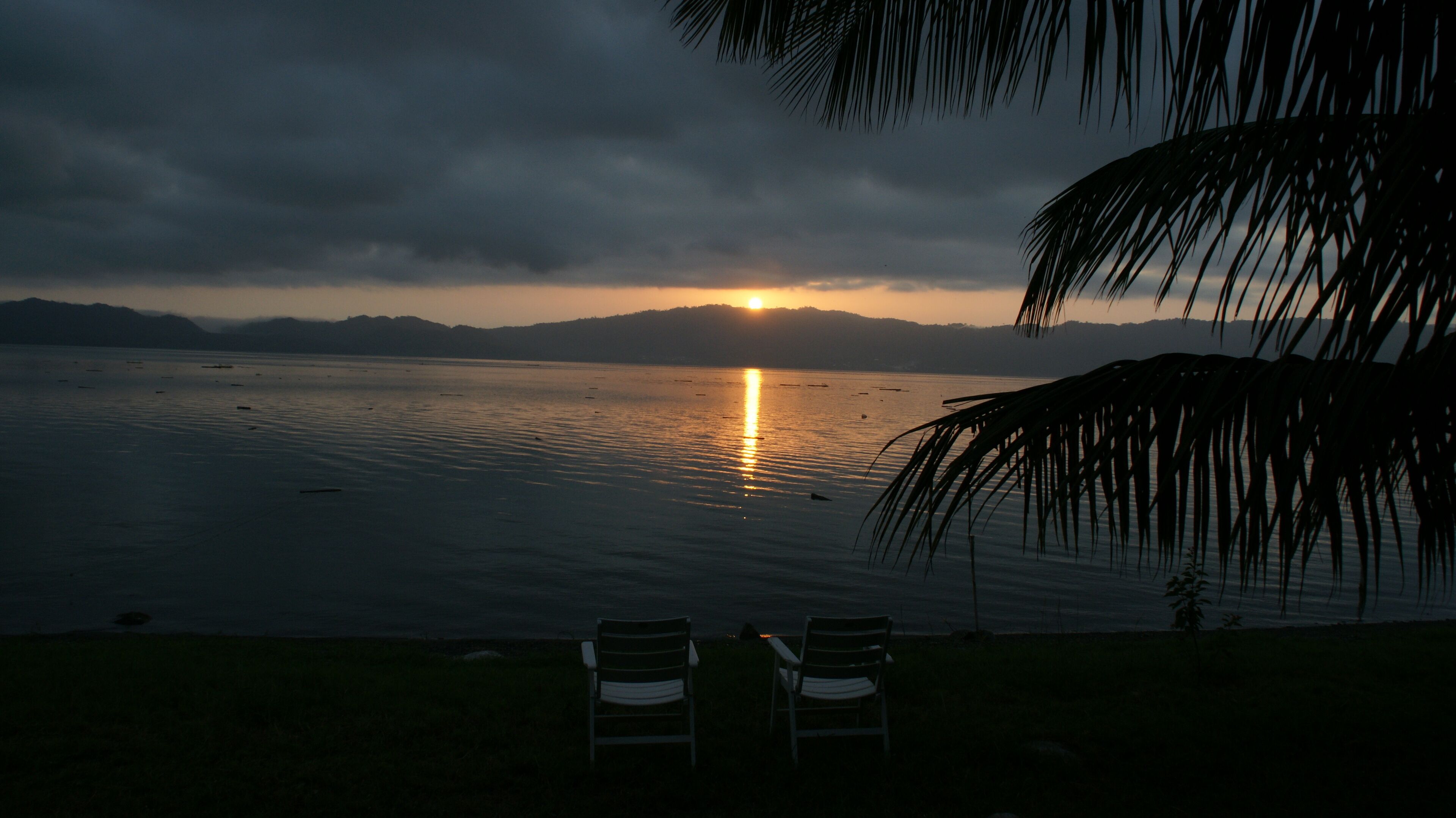 A sunset over a calm body of water with chairs facing the view.