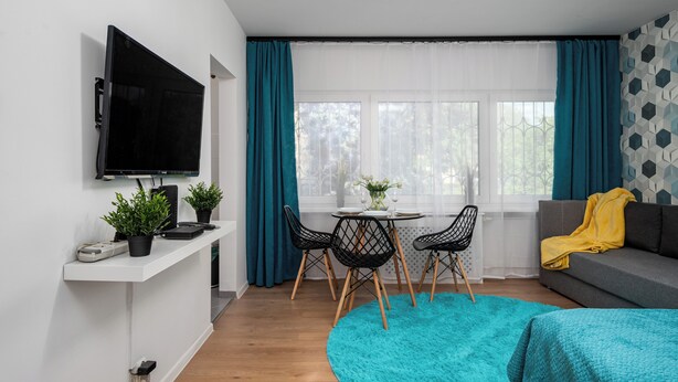 A modern living room with a flat-screen TV, a dining table with chairs, a sofa, and a large window with curtains. - Apartamenty Sun & Snow Kasprowicza Warszawa (Warsaw)