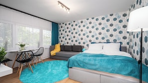 A modern bedroom with a bed, a sofa, a dining table with chairs, and a large window. - Apartamenty Sun & Snow Kasprowicza Warszawa (Warsaw)