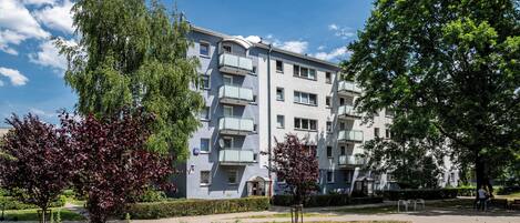 Un edificio residencial de varios pisos con balcones, rodeado de árboles y un césped cuidado.