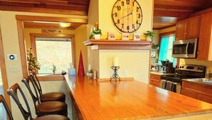 Interior de madera con barra, sillas de madera, un reloj y cocina equipada con microondas y estufa.