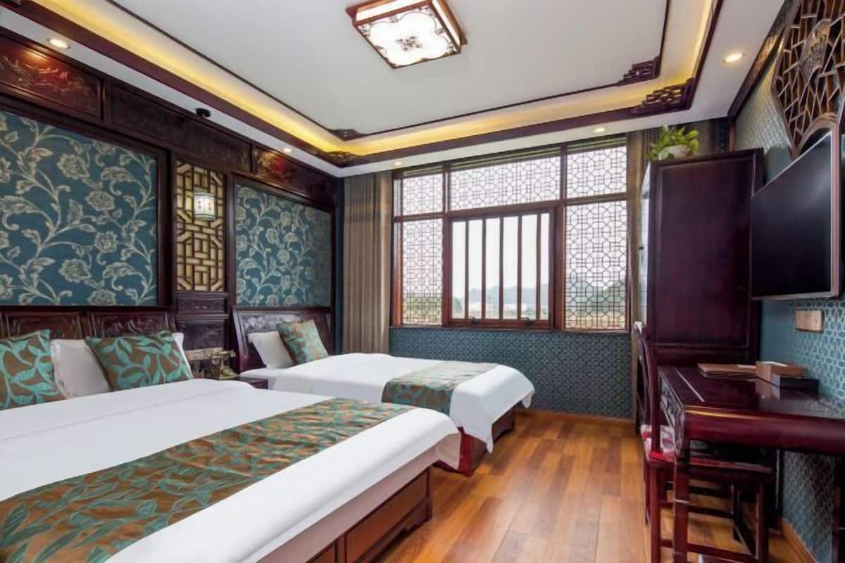 A hotel room with two beds, a TV, a desk, and a window with decorative lattice.