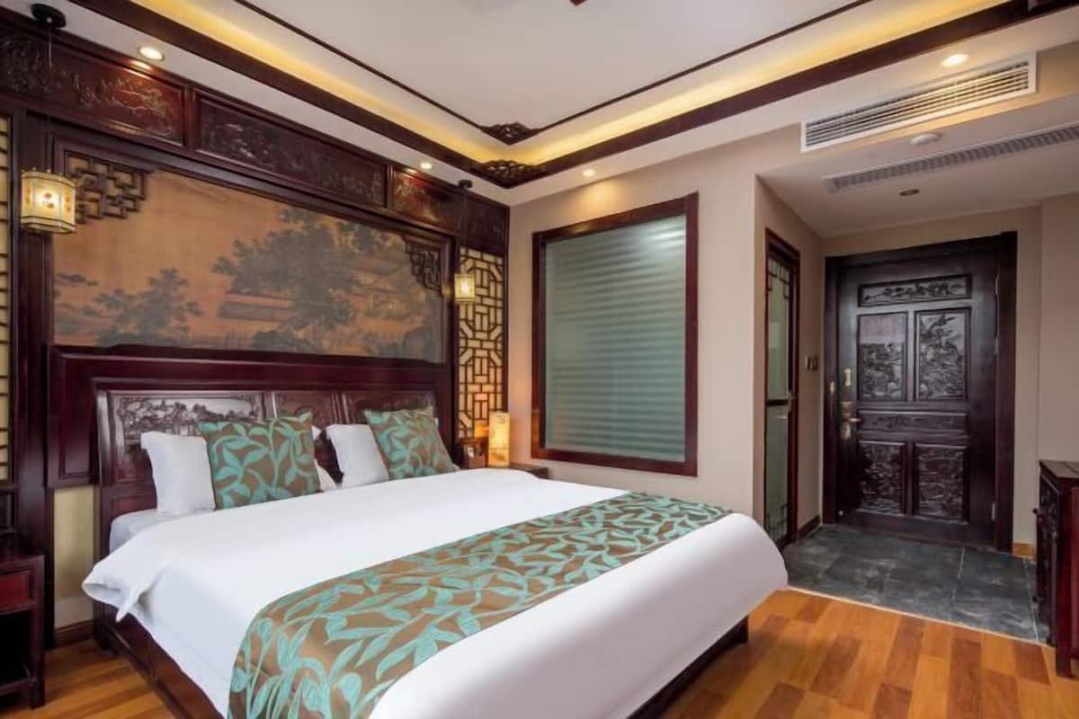 A hotel room with a large bed, wooden headboard, and a traditional Chinese-style wall painting.