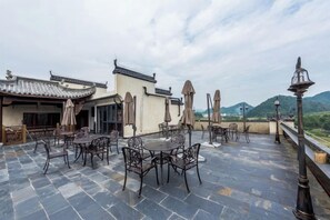 An outdoor patio with tables and chairs, a traditional building with a tiled roof, and a mountainous backdrop. - Siximingyuan in Wuyuan (Wuyuan)