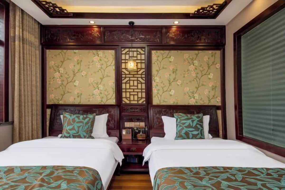A hotel room with two beds, floral wallpaper, a traditional wooden headboard, and a decorative wall panel.