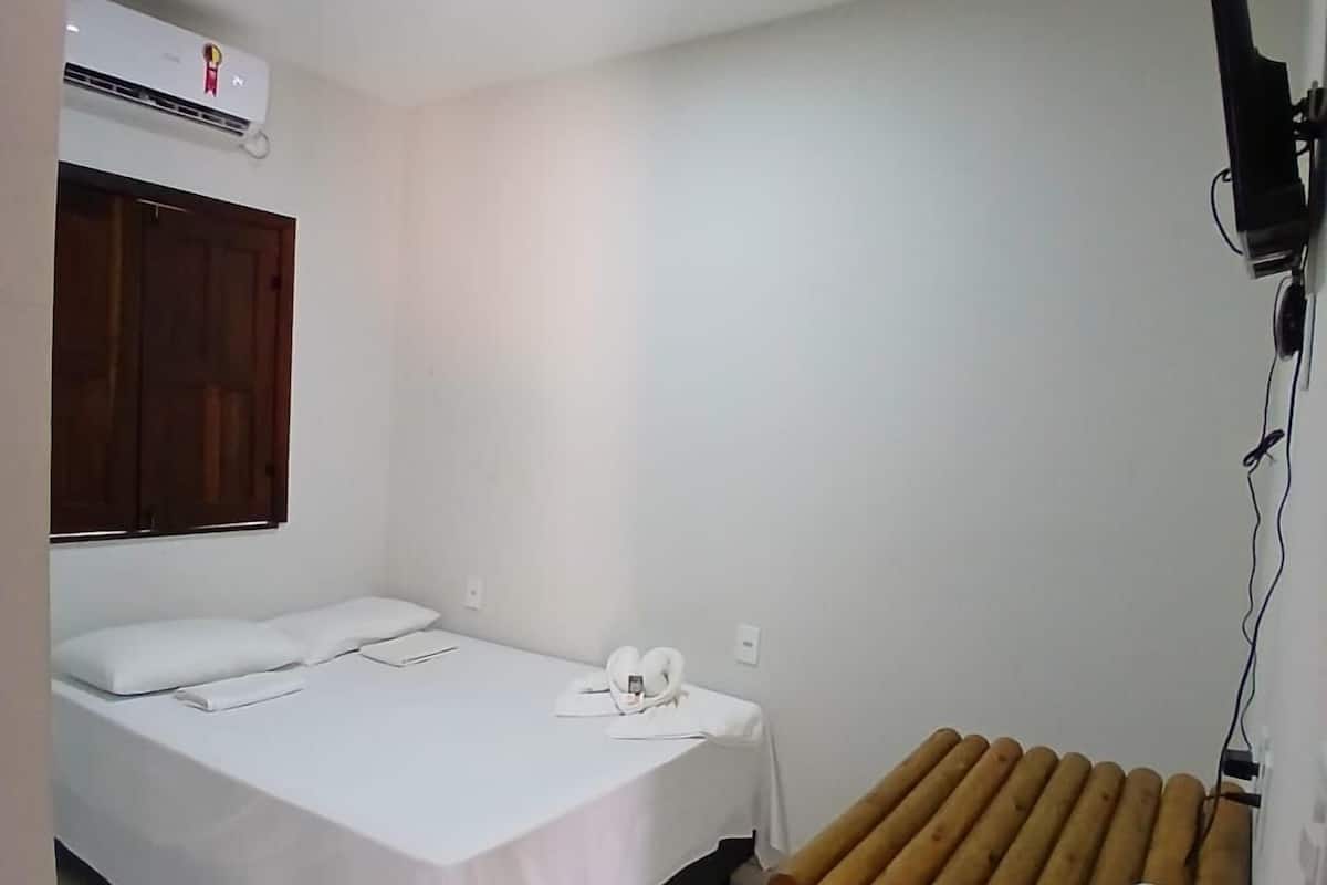 A hotel room with a bed, a desk, a chair, a TV, and a heater.