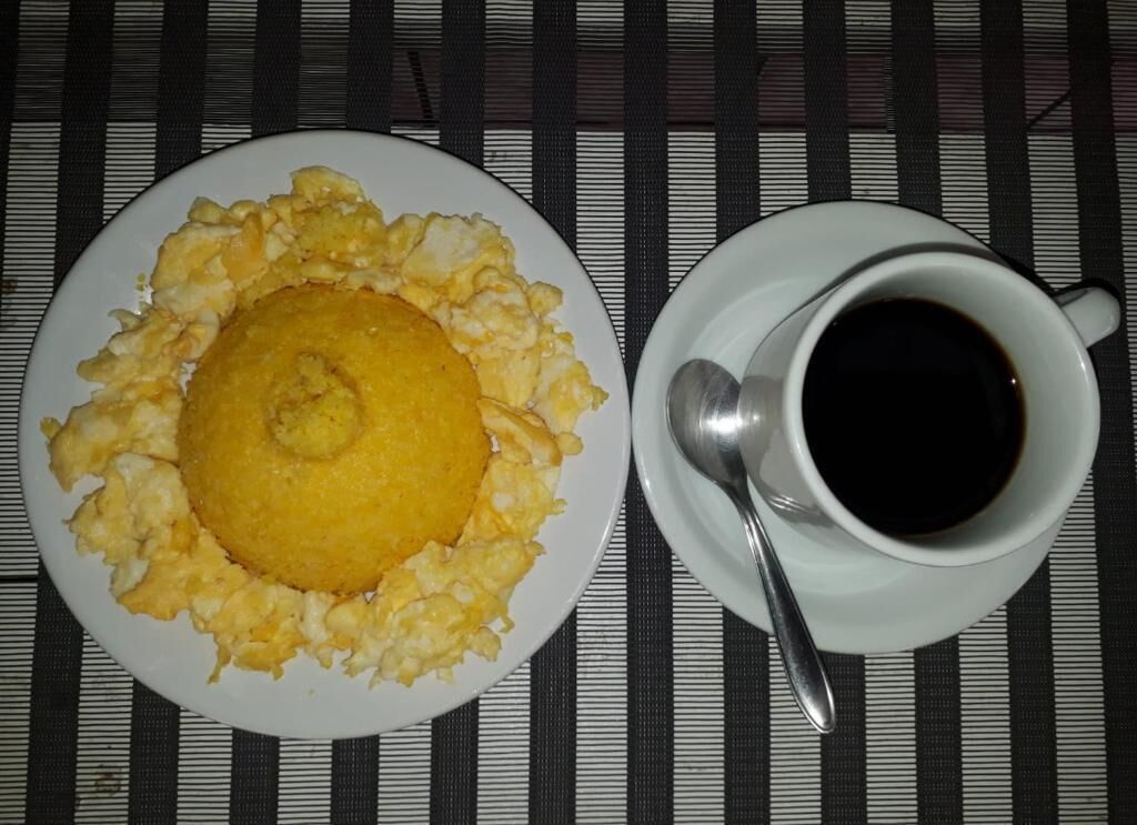 Un plato de huevos revueltos y una taza de café negro sobre un mantel a rayas.