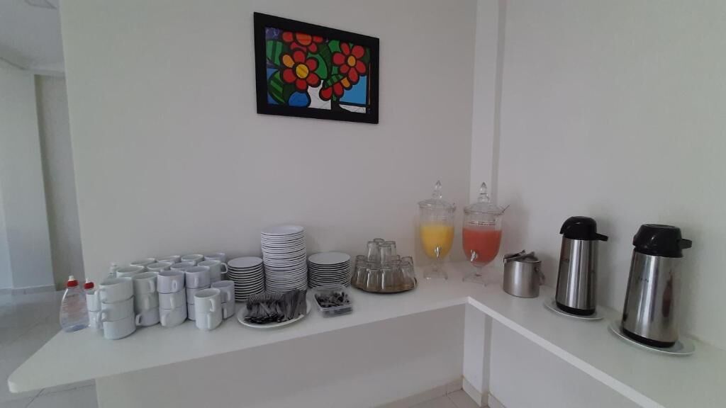 Un bar de petit-déjeuner avec des assiettes empilées, des tasses, des distributeurs de jus et des machines à café.
