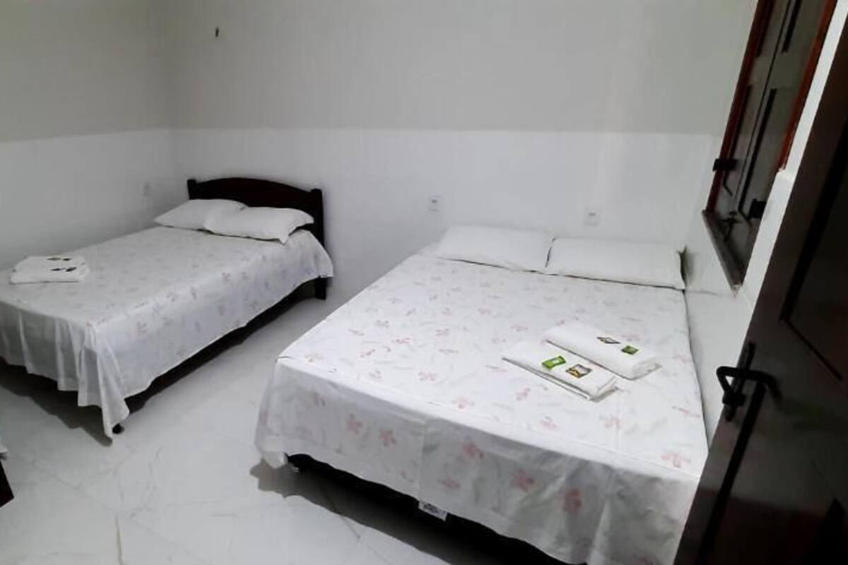 A room with three single beds, each with a white bedspread and pillows. There is a small table with a white tablecloth in the foreground.