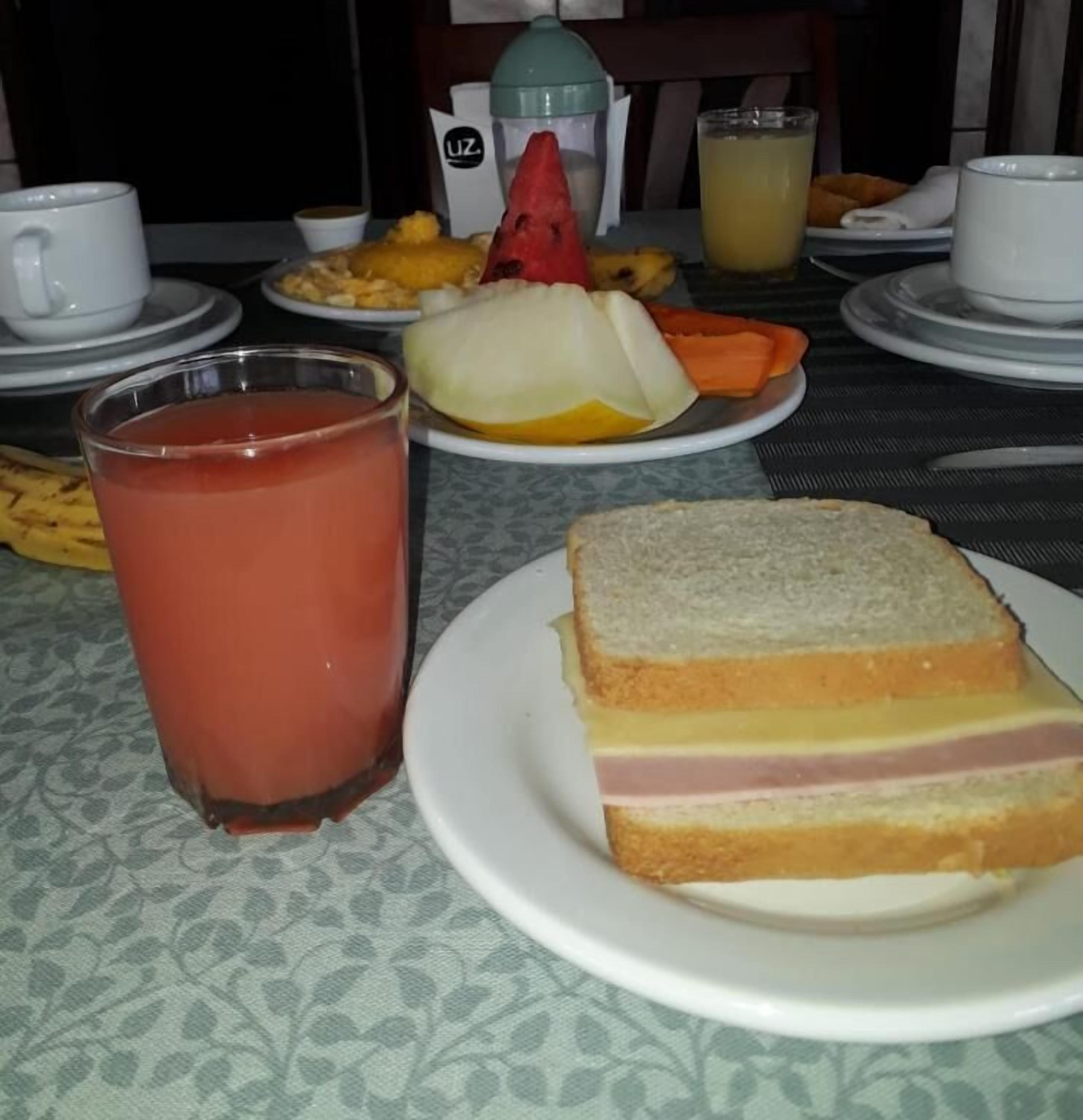 Een maaltijd bestaande uit een belegd broodje, fruit en een glas sap op een tafel.