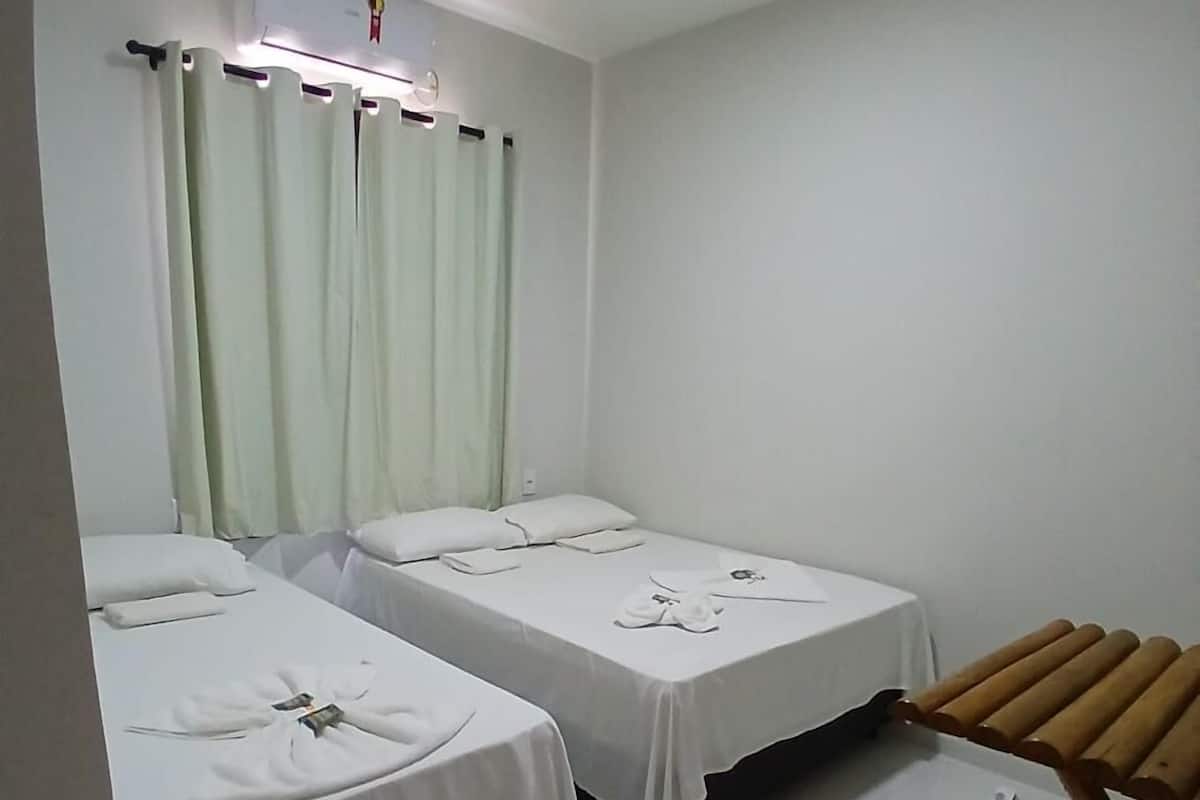 A room with two beds, a small table, a wooden chair, and an air conditioning unit.