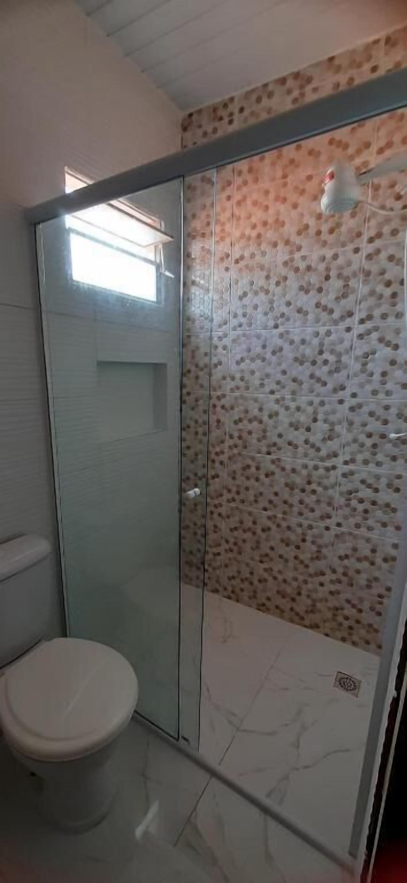 A bathroom with a toilet, a shower with a glass door, and a tiled wall.