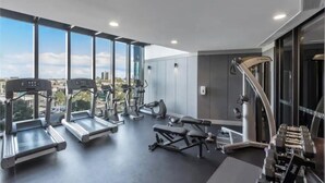 Ein modernes Fitnessstudio mit Laufbändern, Kraftgeräten und einem Rudergerät, ausgestattet mit großen Fenstern und Blick auf die Stadt.