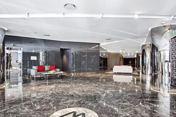 A modern lobby with a marble floor, a sofa with red cushions, and a patterned wall.