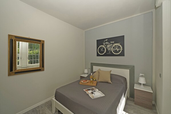 Une chambre à coucher comprenant un lit, une table de chevet, une lampe, une fenêtre encadrée et une illustration de vélo accrochée au mur.