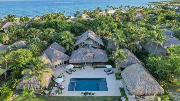 Vue aérienne d’un complexe hôtelier tropical, avec ses bungalows aux toits de chaume, sa piscine et sa végétation luxuriante.
