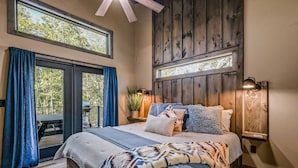 A bedroom with a large bed, wooden walls, and a view of trees through the windows.
