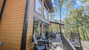 A wooden building with a deck, outdoor seating, and large windows.