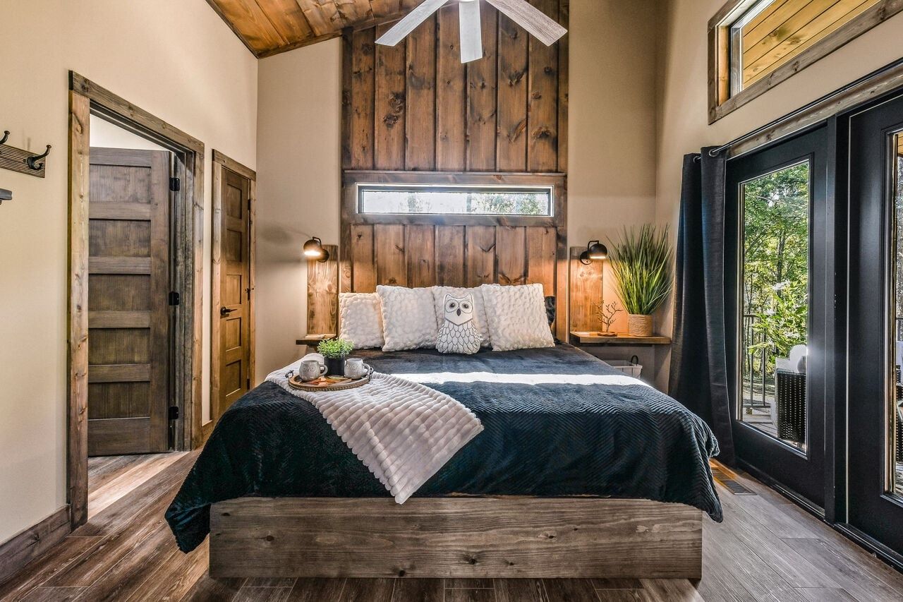 A bedroom with a bed, wooden walls, a window, and a view of the outdoors.