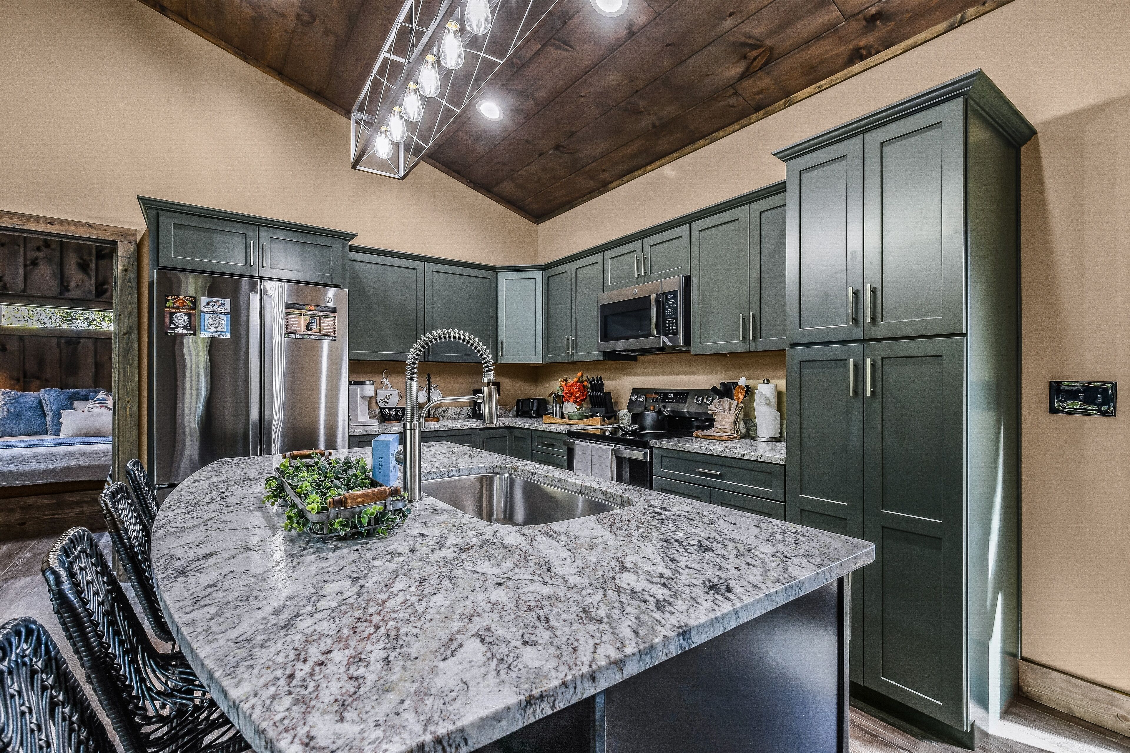A kitchen with dark green cabinets, stainless steel appliances, a marble countertop, and a wooden ceiling.