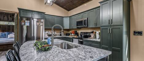 A kitchen with dark green cabinets, stainless steel appliances, a marble countertop, and a wooden ceiling.