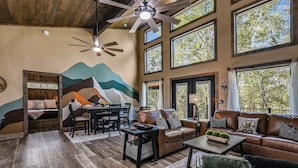 A spacious living area with a high ceiling, multiple windows, a ceiling fan, and a mural on the wall.