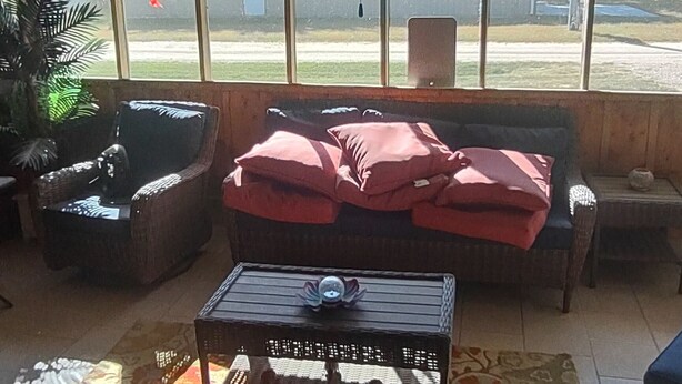 Un porche techado con mobiliario de mimbre, una mesa y una alfombra estampada.