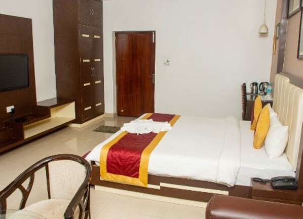 A hotel room with a bed, a TV, a wardrobe, and a desk with a lamp.