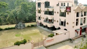 Un hotel de varios pisos con balcones, una señal que indica que es un hotel, y un patio empedrado con una pequeña zona ajardinada.