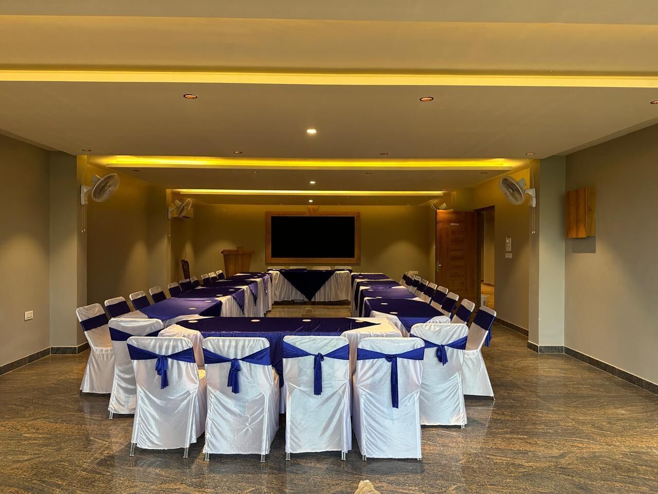 A conference room with a long table, chairs with blue sashes, and a projector screen.
