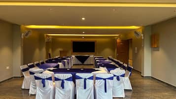 A conference room with a long table, chairs with blue sashes, and a projector screen.