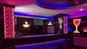 A bar area with a neon sign, a glass display, and a patterned wall. - Pinky Hotel (Dausa)