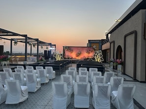 An outdoor seating area with rows of chairs, a stage with floral decorations, and a view of the sky. - Pinky Hotel (Dausa)
