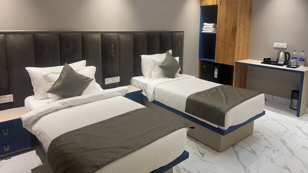 A modern hotel room with two single beds, a wooden wardrobe, a desk with a kettle, and a trash bin. - Pinky Hotel (Dausa)